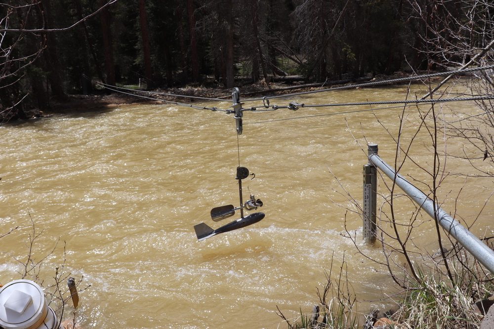 Current meter suspended on a cableway measuring discharge on a high, sediment-laden river