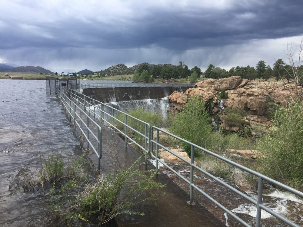 Reservoir spillway flowing under storm clouds during spring runoff